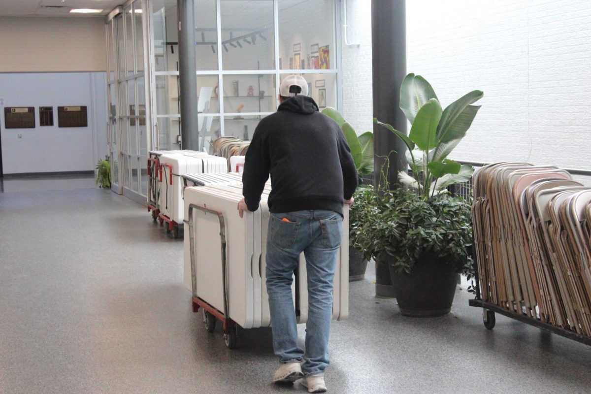 Building Manager Weslie Harbit moves table along a hallway. While Mr. Harbit has worked as Building Manager for the last nine years, he first started only coming in as a "weekend person" before his promotion. "My main job is to maintain the forty-four acres that we sit on. I'm in charge of eighteen custodians. That's including myself."